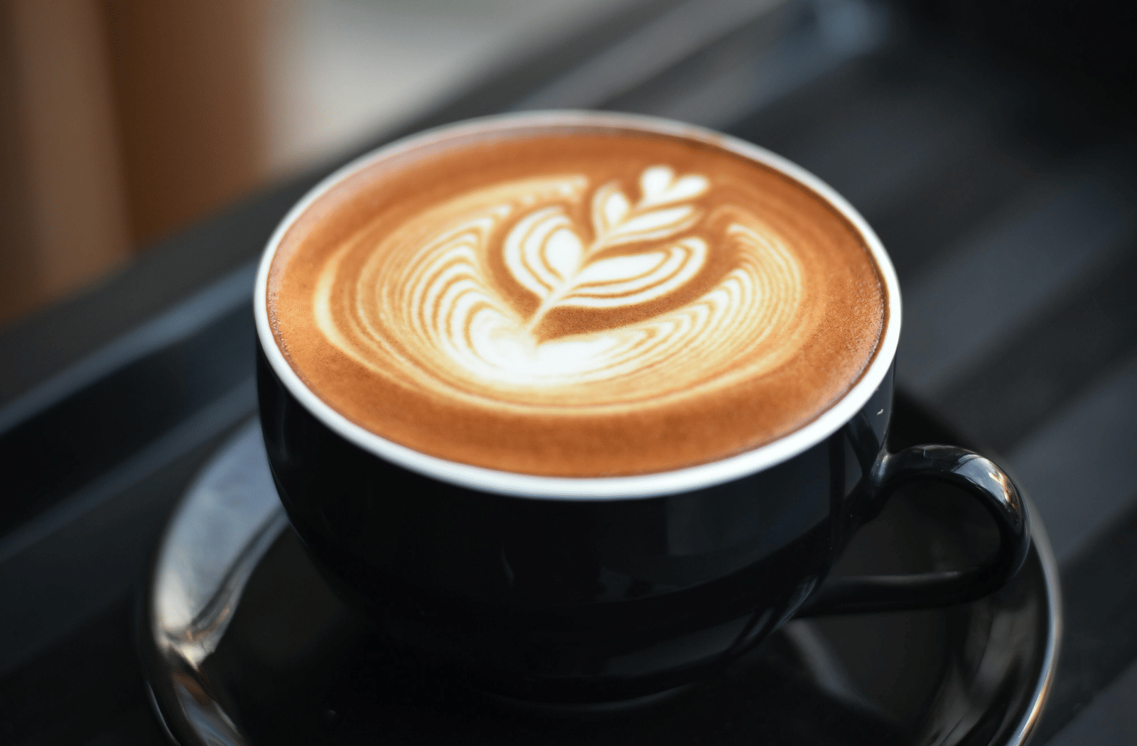 Cup of coffee with latte art served in a black cup and saucer on a tray in a cafe setting