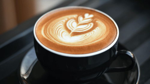 A cup of coffee with latte art on a saucer and tray, with a blurred background.