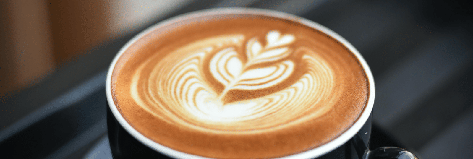 Cup of coffee with latte art served in a black cup and saucer on a tray in a cafe setting
