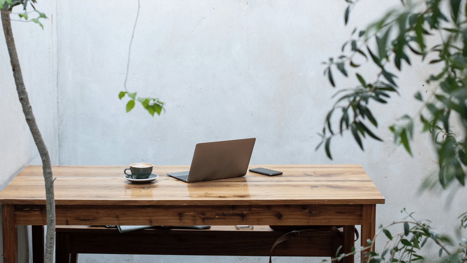 A view of a wooden table outdoors with a laptop on top of it and the background engulfed by a thick fog.