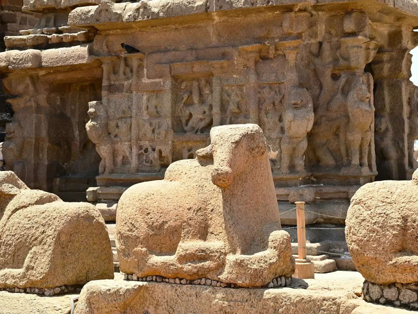 A tall, multi-tiered stone temple with intricate carvings, standing under a bright sky, possibly the Shore Temple.