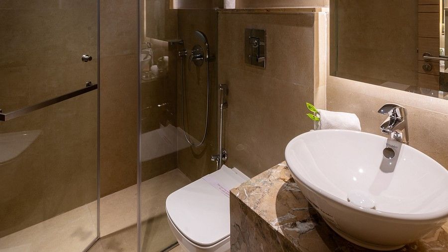 A hotel bathroom with a sleek design, featuring a glass shower enclosure, wall-mounted sink, and warm, soft lighting at Hotel Saket 27, New Delhi