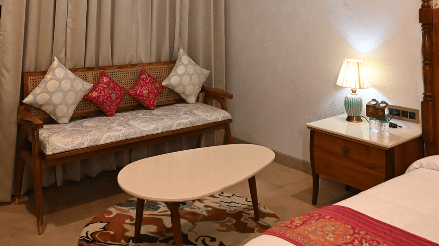 A seating nook at Kadamb Kuteer with a brown armchair and a small round table set against a window with floor-to-ceiling decorative drapes.