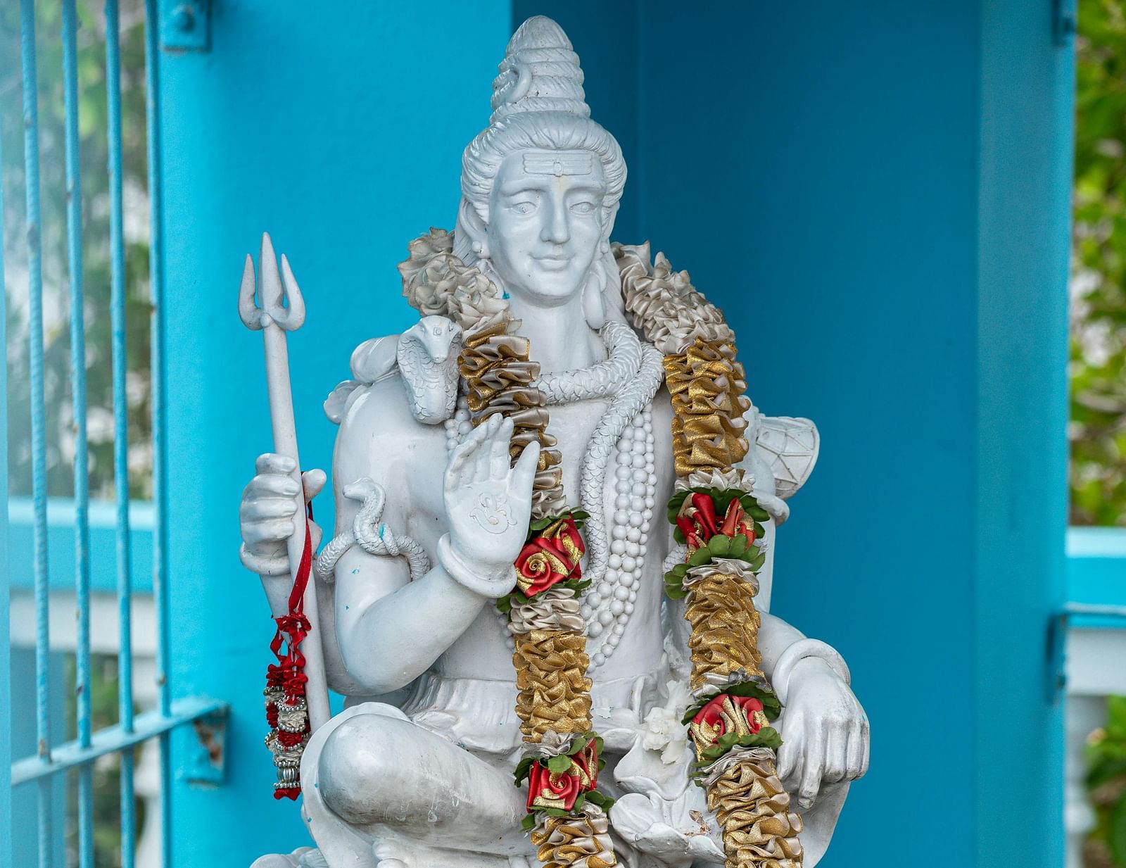 a statue made of white marble of lord Shiva with a dried flower garland put around his neck
