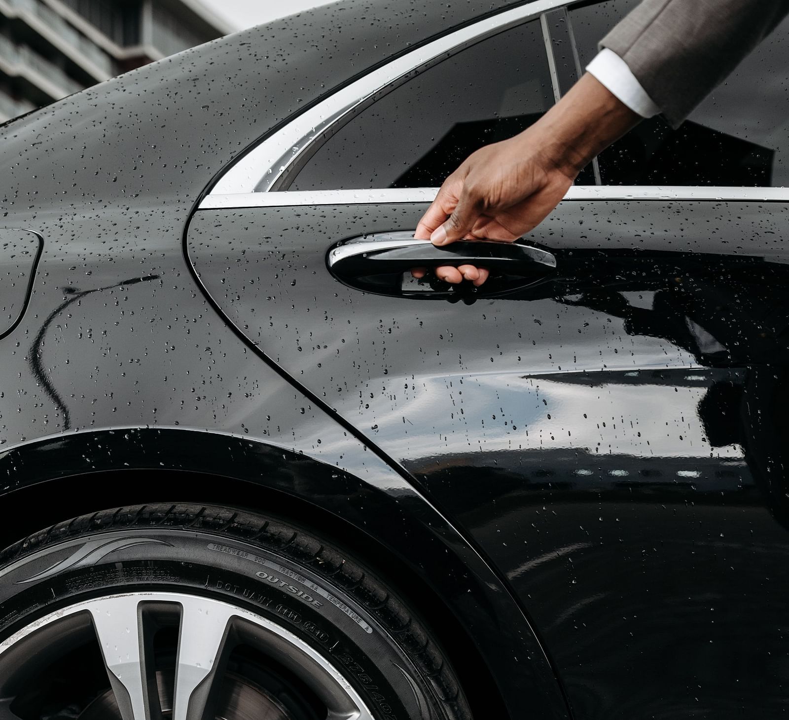 A person in a suit opening a car door of a modern black car