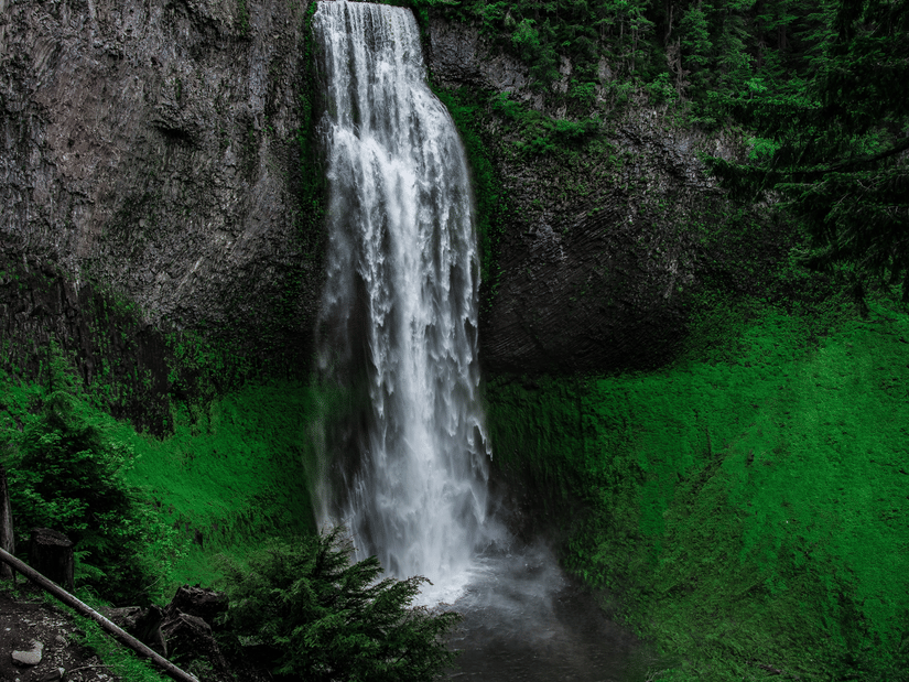 A view from below of Kune Waterfalls cascading from in between two peaks and numerous trees seen above them