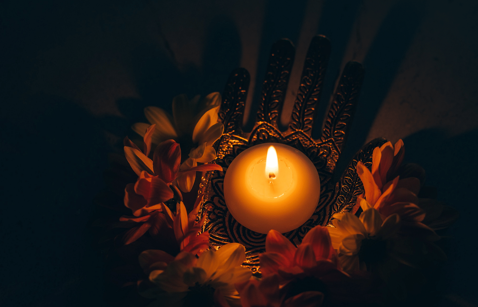 A round candle lit, surrounding with different flowers, kept on a metal plate.