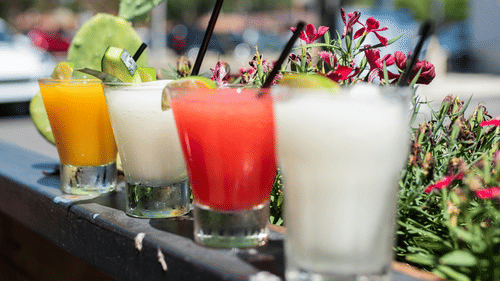 Four glasses of cocktails kept on a ledge with a tree in the background