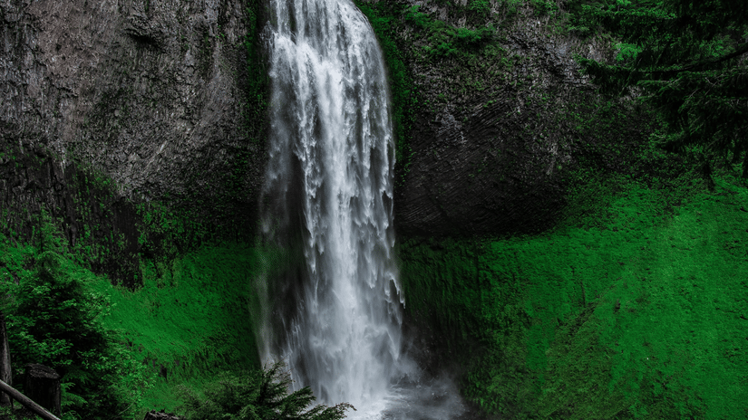 A view from below of Kune Waterfalls cascading from in between two peaks and numerous trees seen above them