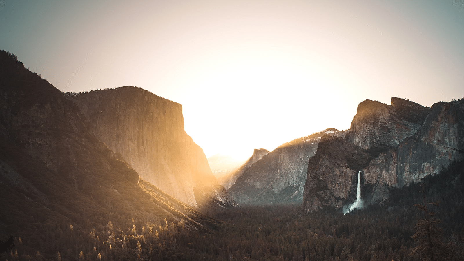 a view of the sunrise from between the gap in the mountains with sun rays falling on the trees below