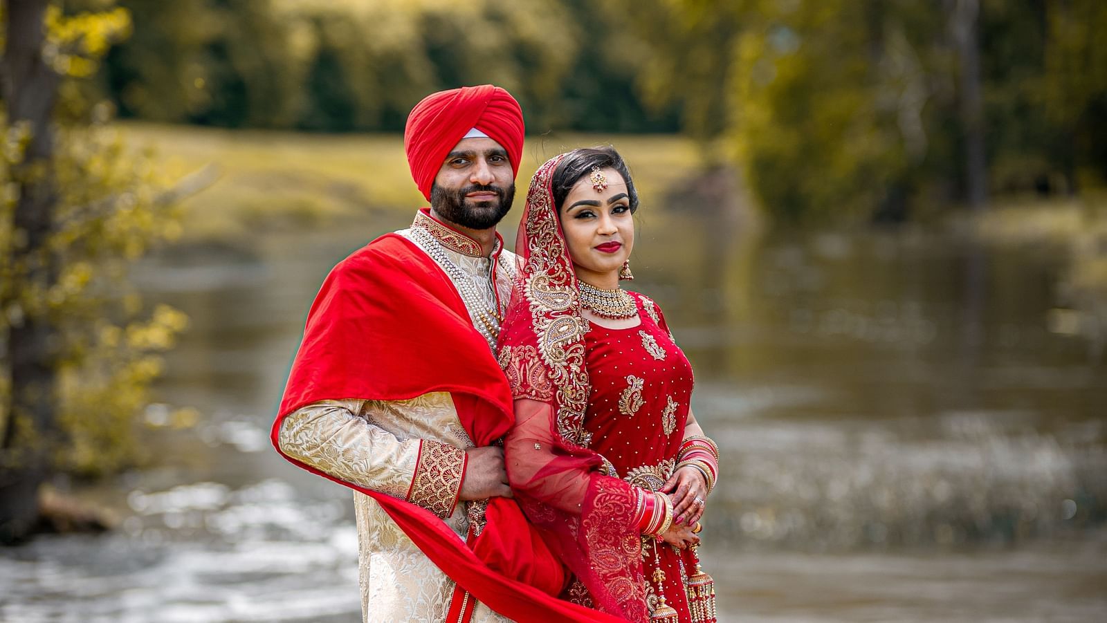 a bride and groom poses against the backdrop of greenery