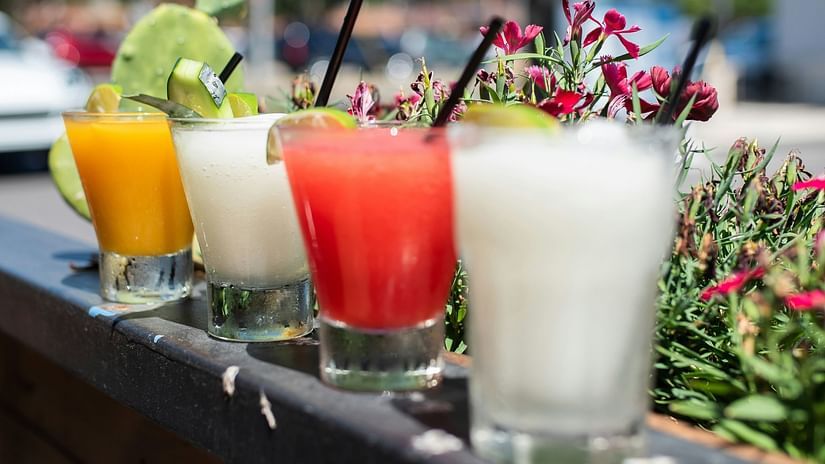 Four glasses of cocktails kept on a ledge with a tree in the background