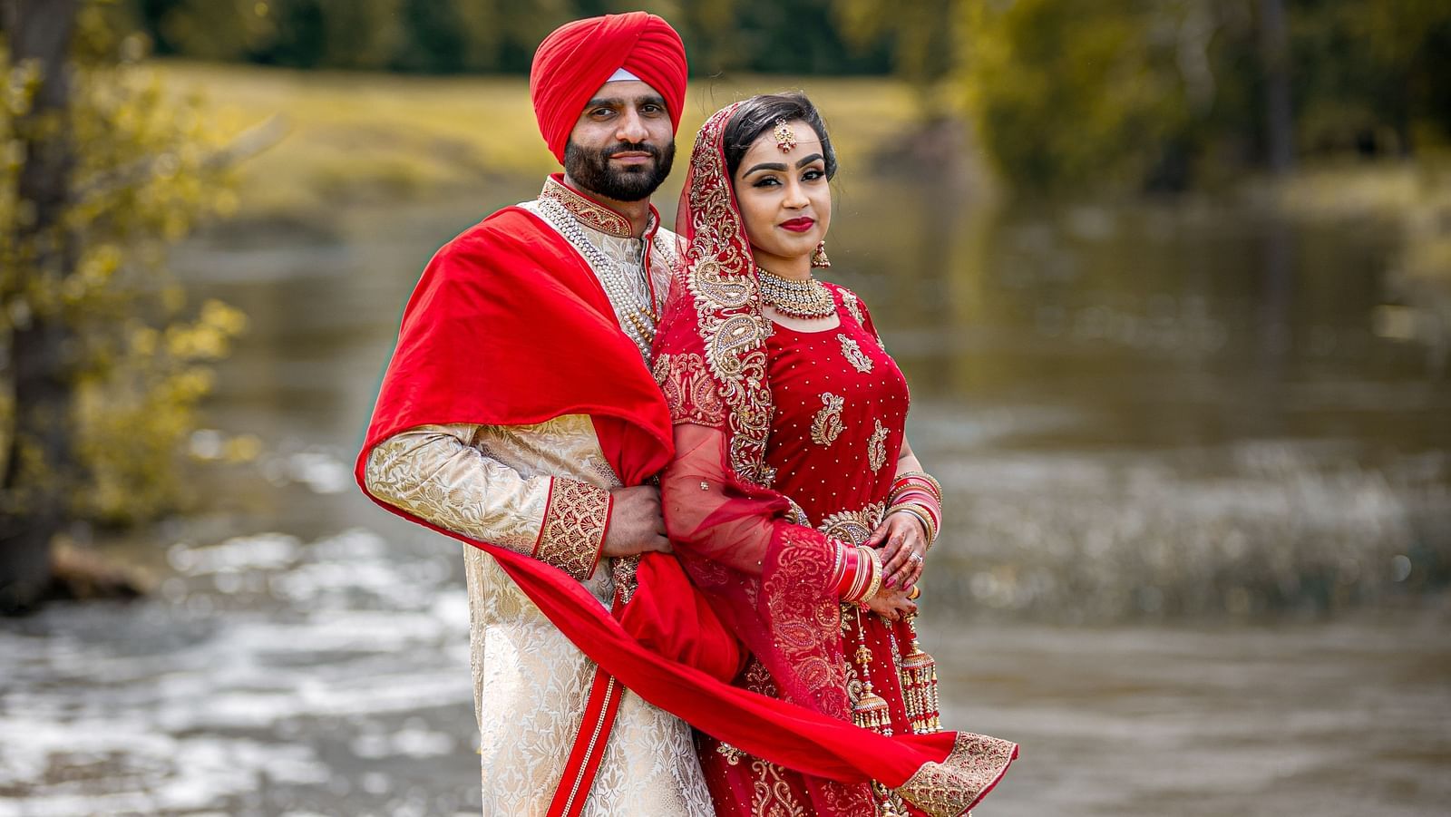 a bride and groom poses against the backdrop of greenery