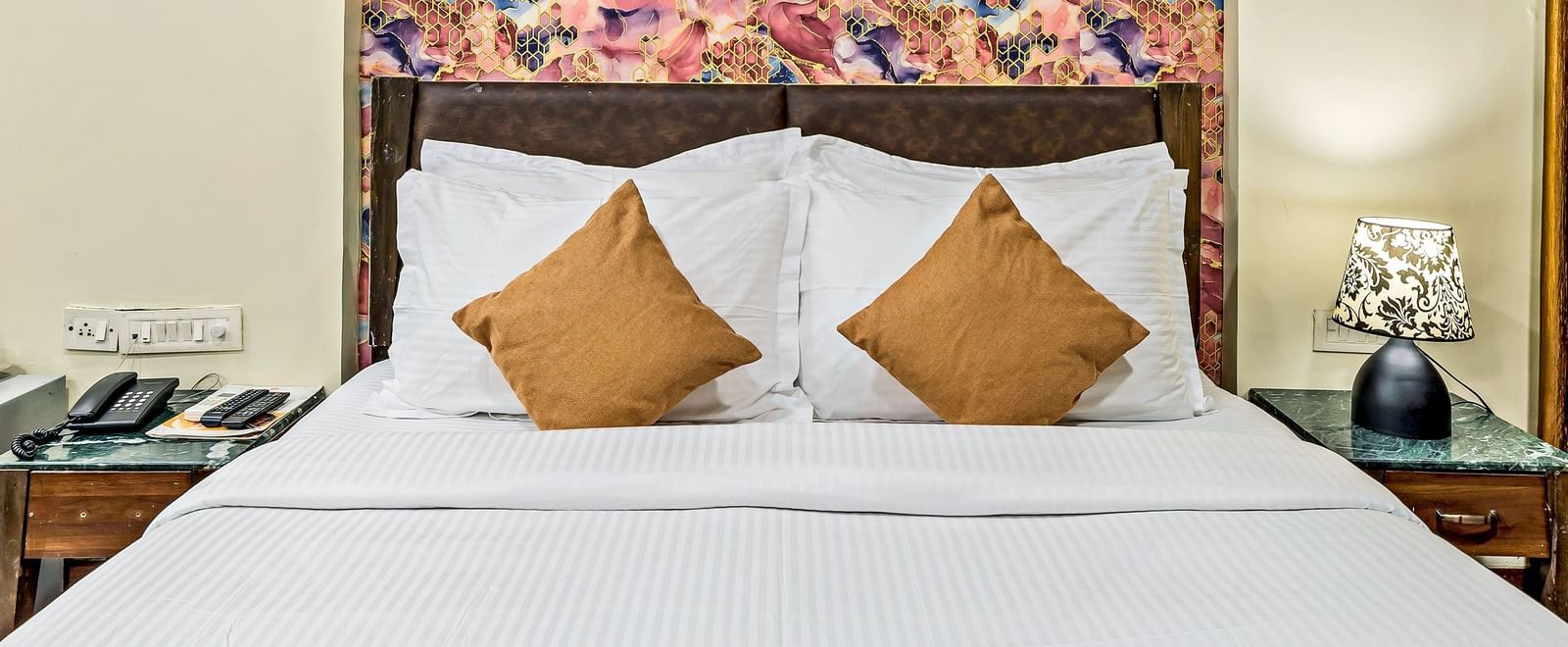 A royal executive room in Krushnai Resort with a double bed made with white linen and yellow runner, and a painting hanging on the wall.