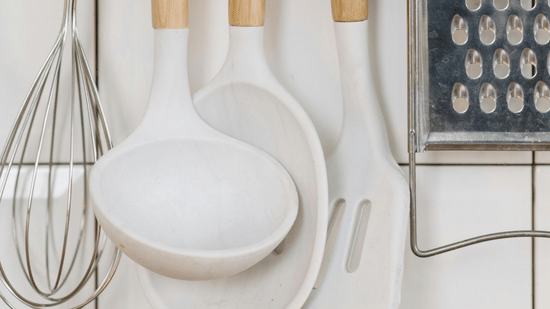 A view of kitchen utensils, including rolling pins and a whisk, hanging on hooks against a tiled wall.