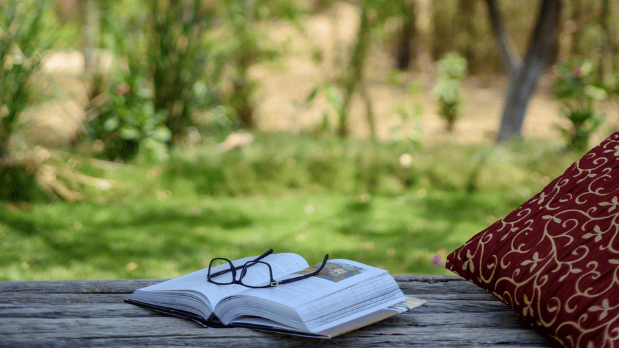 An open book with spectacles placed on it beside a red cushion | The Riverwood Forest Retreat, Pench