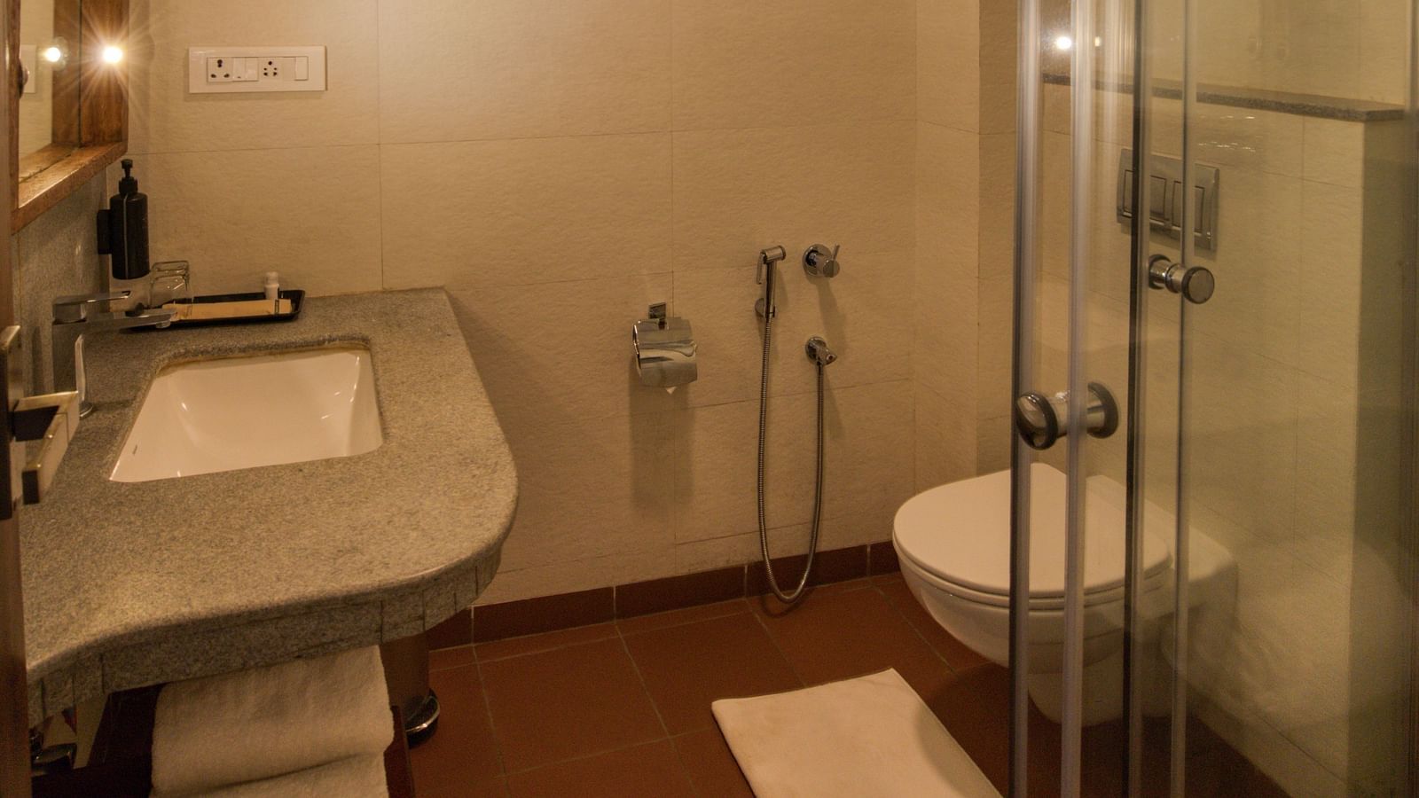 Modern bathroom with glass-enclosed shower, white fixtures, and warm lighting. | Mango Hill, Yercaud