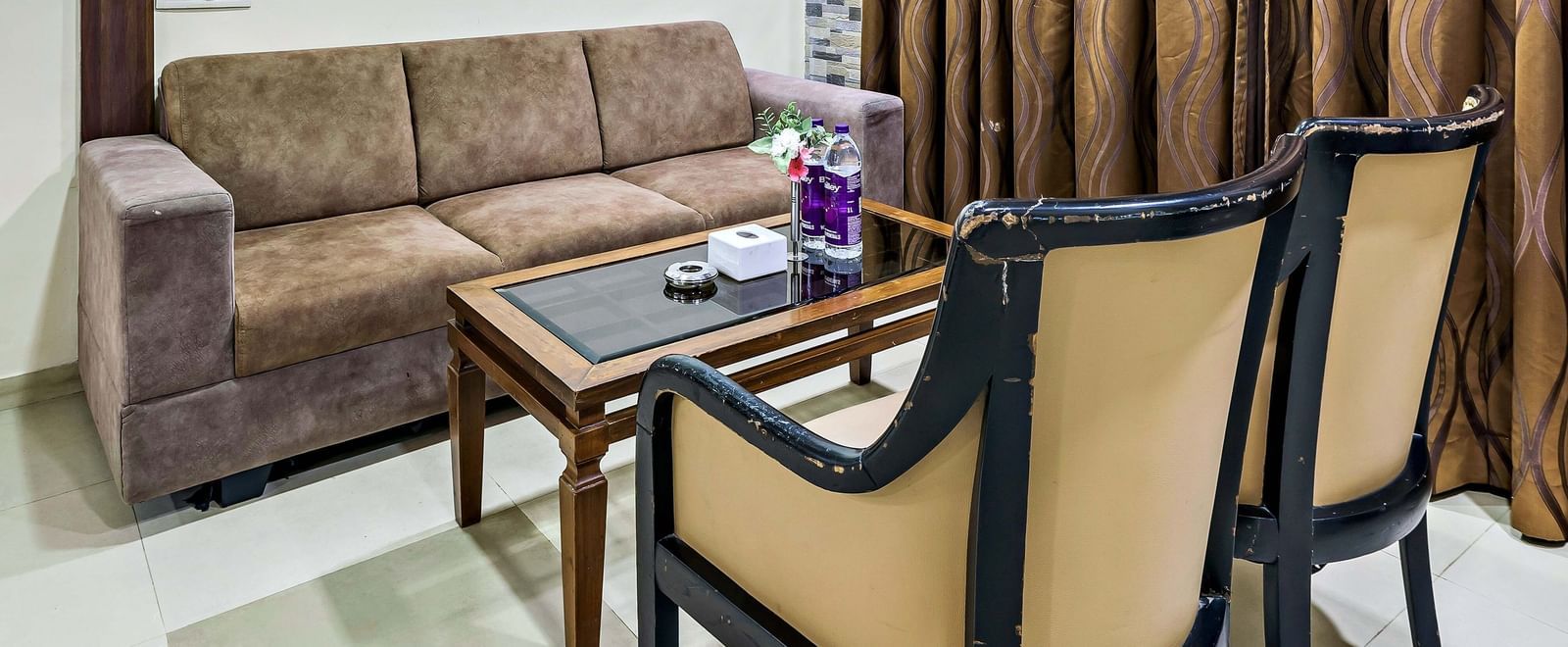 A suite in Krushnai Resort featuring a couch and 2 lounge chairs near a window with its drapes closed.