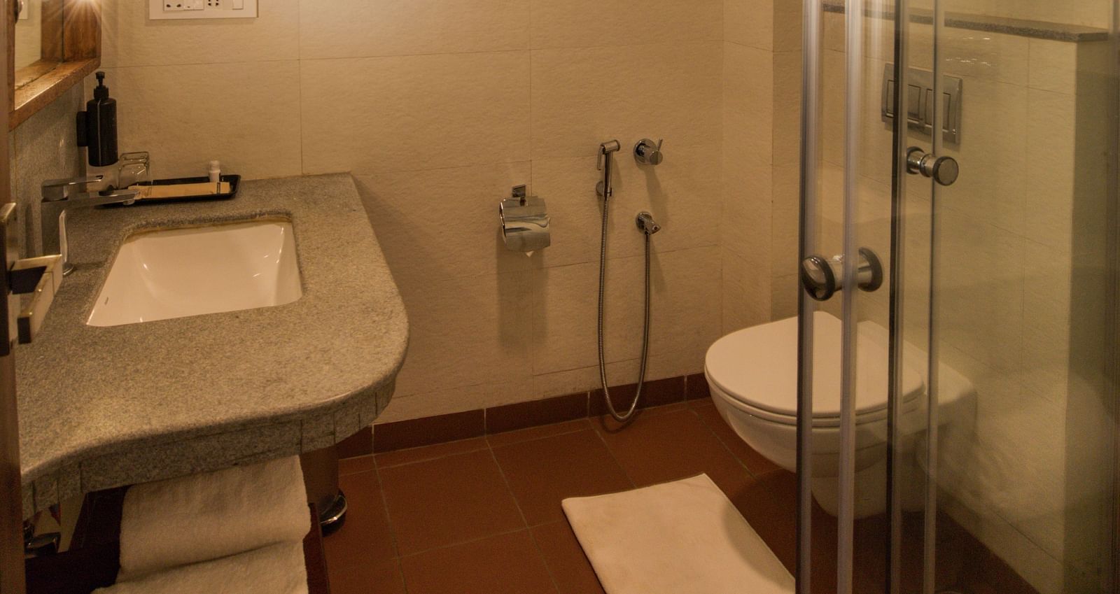 Modern bathroom with glass-enclosed shower, white fixtures, and warm lighting. | Mango Hill, Yercaud