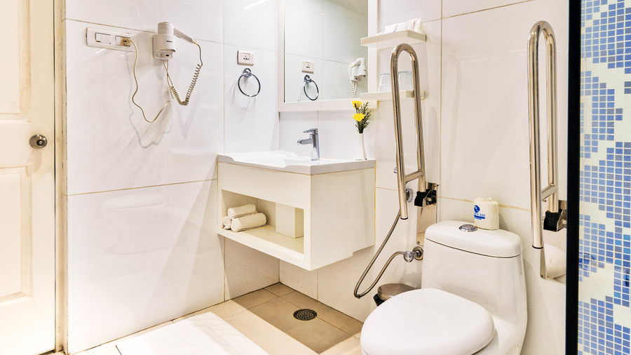 White tiled bathroom with toilet, sink, mirror, and shower area at Grande Bay Resort & Spa, Mamallapuram.