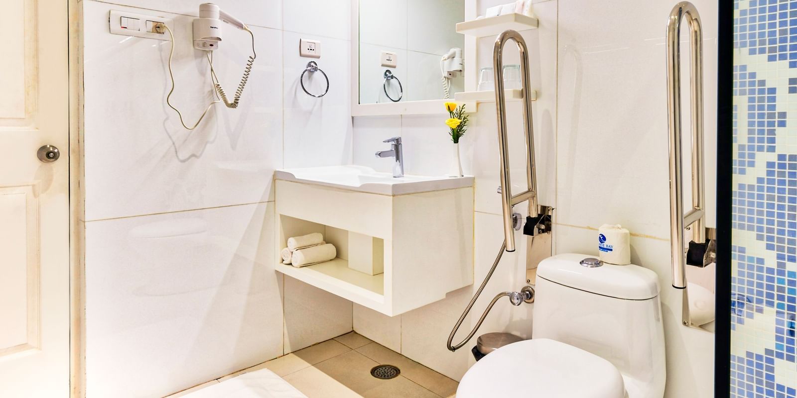 White tiled bathroom with toilet, sink, mirror and shower area at Grande Bay Resort & Spa.