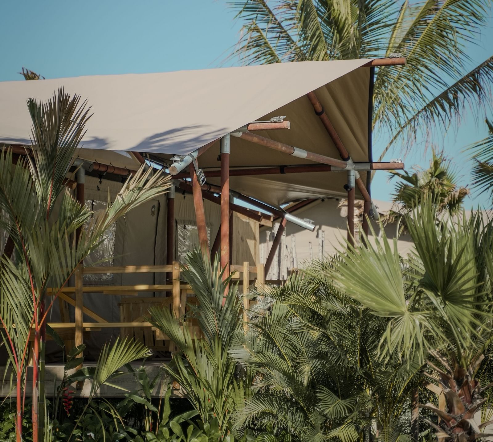 A corner view of the Grateful Tent at WoCAL Retreat Ke Ga nestled in dense tropical greenery, with its canvas roof partially visible through the surrounding foliage.