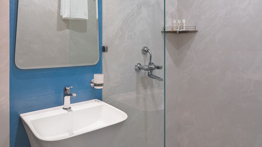 A bathroom with a wash basin, a wall-mounted mirror, and a glass partition separating the shower area | Hotel Ganga Maiya