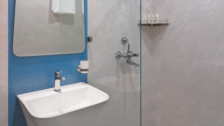 A bathroom with a wash basin, a wall-mounted mirror, and a glass partition separating the shower area | Hotel Ganga Maiya