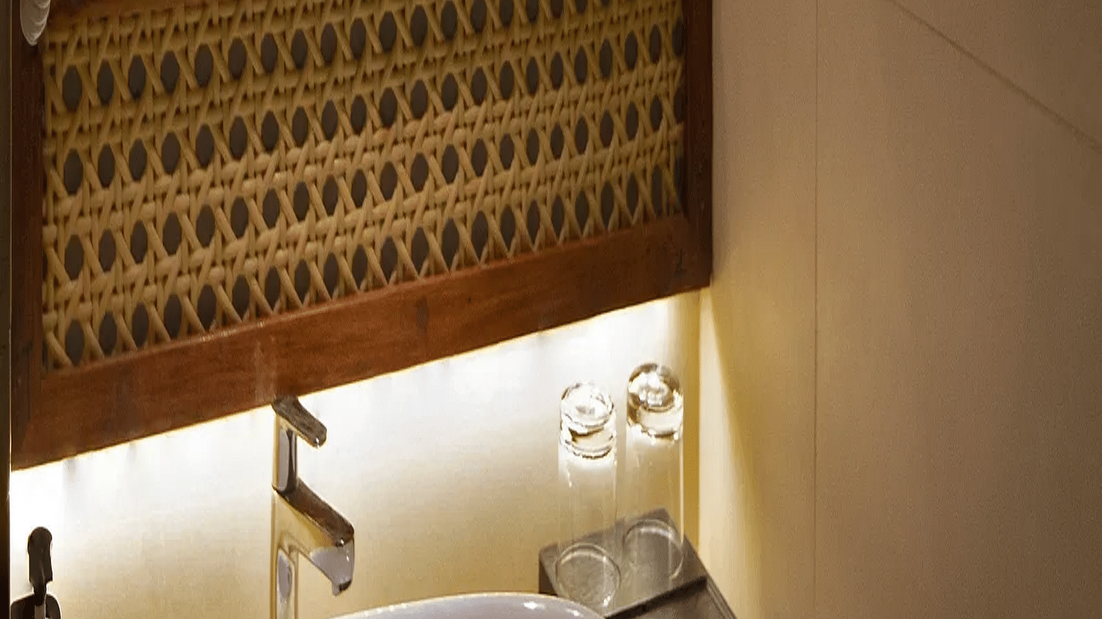 Image of bathroom of Coral Sapphire at Coral Reef Resort and Spa in Havelock in dim lighting featuring a sink and a mirror over it with its background lit up with warm lights 
