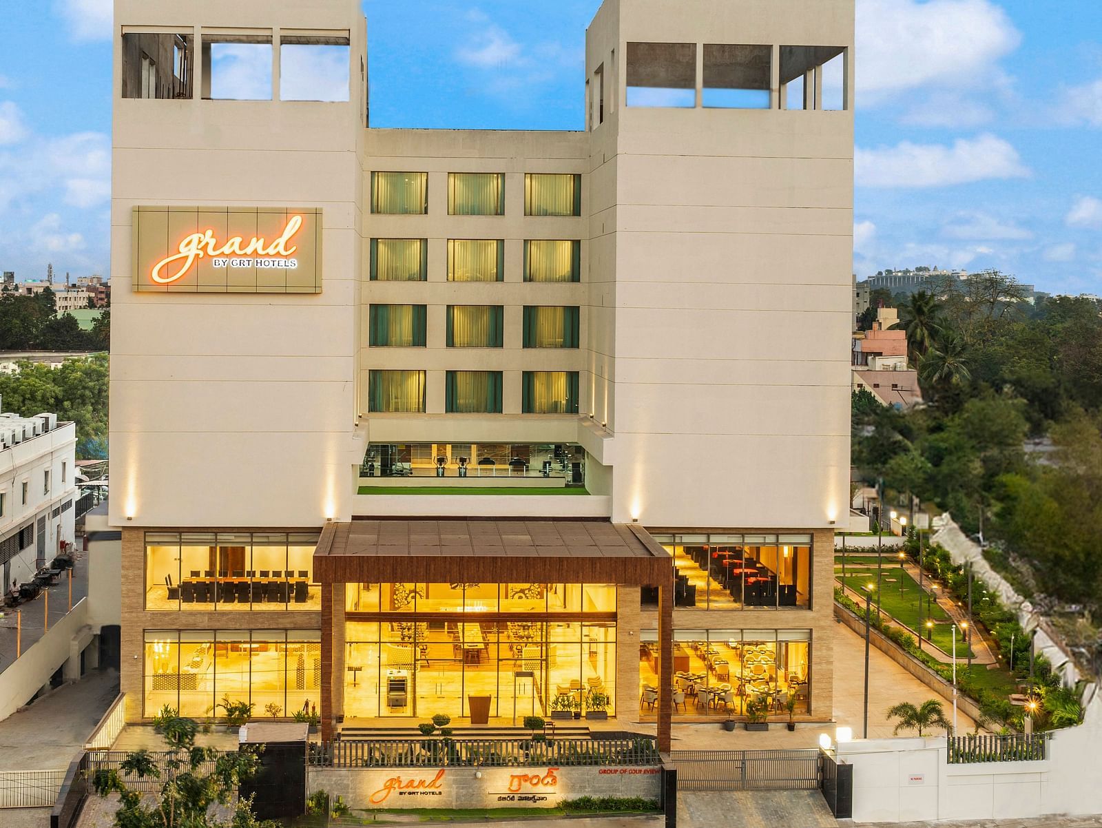 Facade image of Grand Vijayawada by GRT Hotels surrounded by folaige under a blue sky.