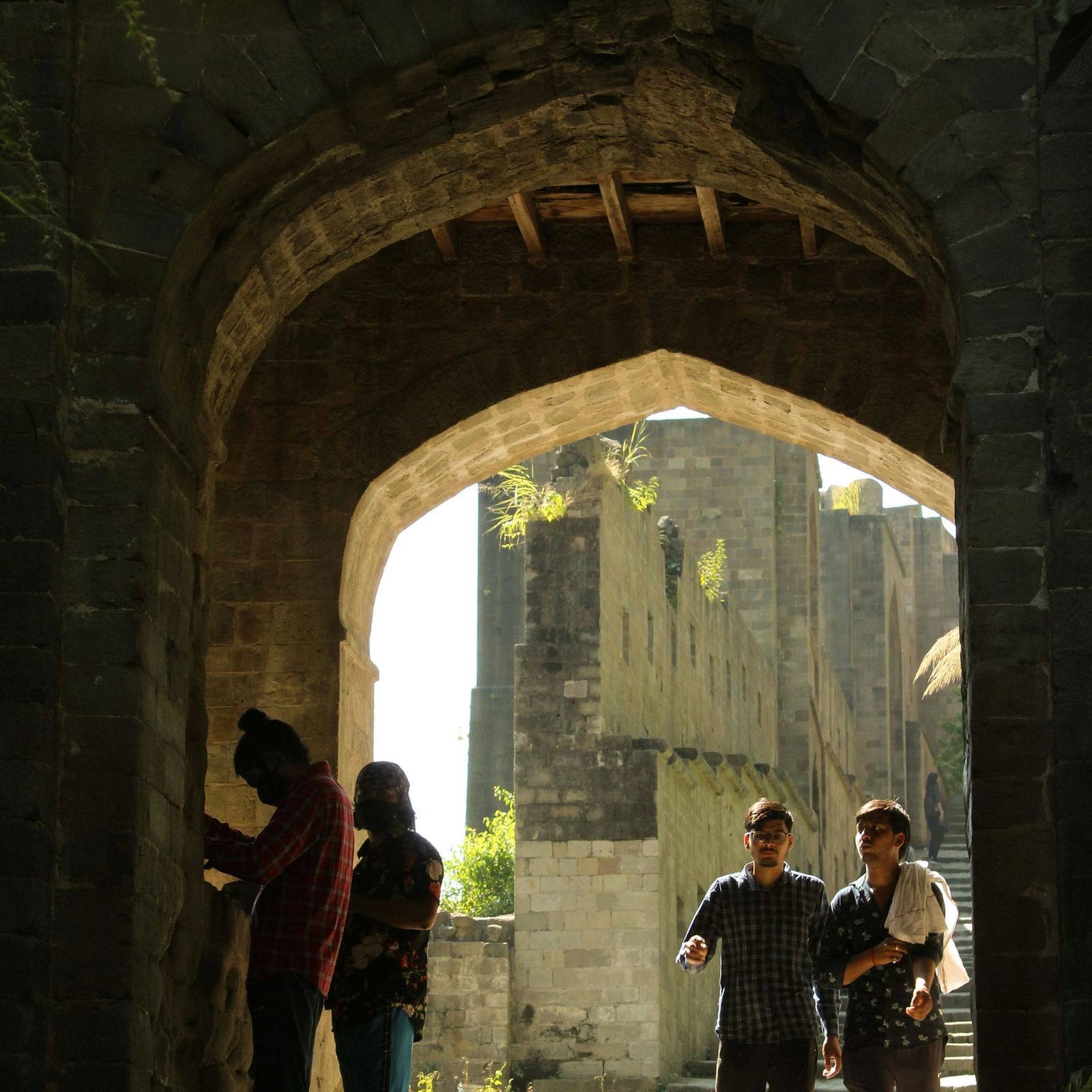 People walking through a historic stone archway of Kangra Fort