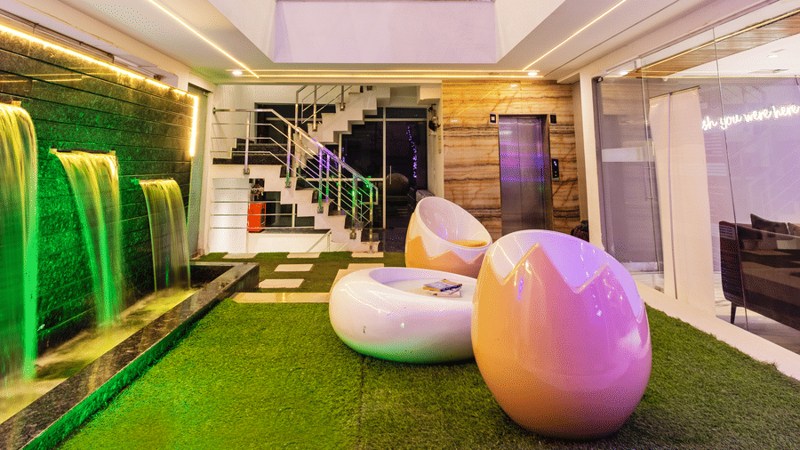 Hotel atrium with broken egg-shaped chairs, artificial grass-flooring, and water fountains at Hotel Bawa, Gurgaon.