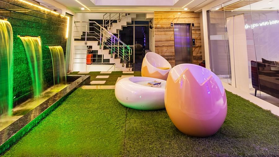 Hotel atrium with broken egg-shaped chairs, artificial grass-flooring, and water fountains at Hotel Bawa, Gurgaon.