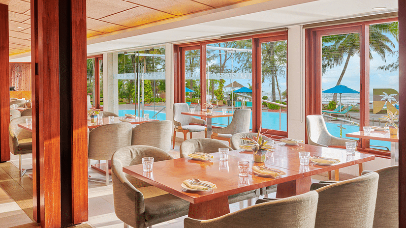 Chairs and tables placed right beside a glass window in a restaurant overlooking the swimming pool outside | The Resort, Mumbai