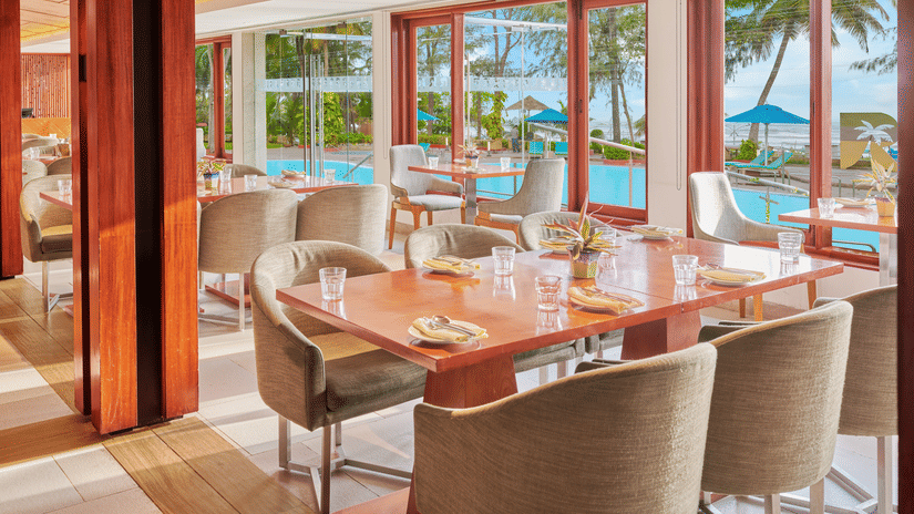 Chairs and tables placed right beside a glass window in a restaurant overlooking the swimming pool outside | The Resort, Mumbai