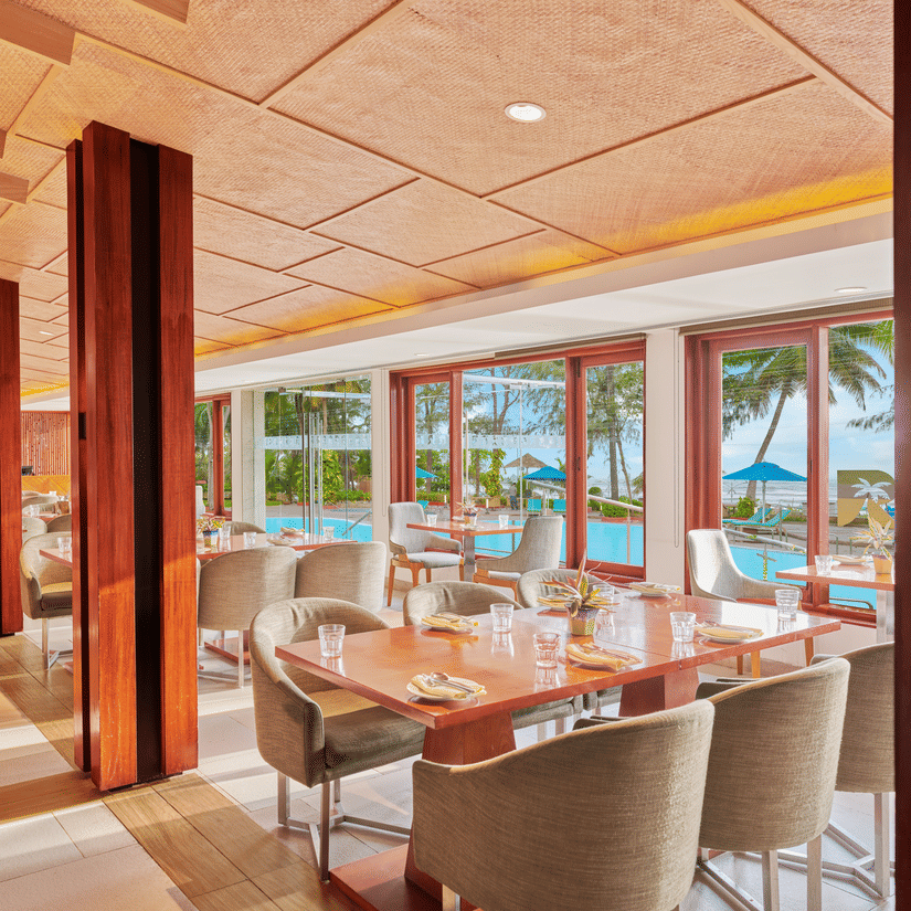 Chairs and tables placed right beside a glass window in a restaurant overlooking the swimming pool outside | The Resort, Mumbai