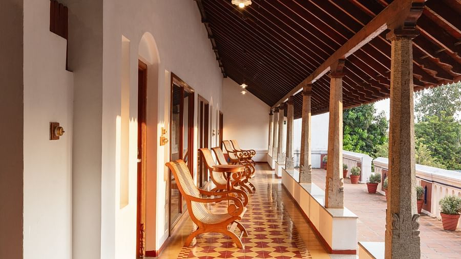 Traditional wooden rocking chairs line a covered veranda with a colorful tile floor at Chidambara Vilas Resort