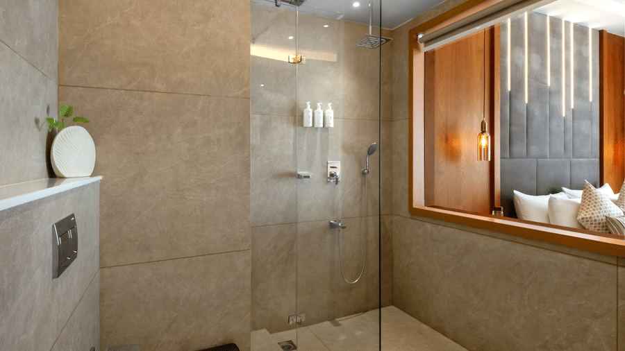 A bright bathroom space featuring a wall hung toilet and a walk in shower behind a clear glass partition wall at Tiara by MPS.