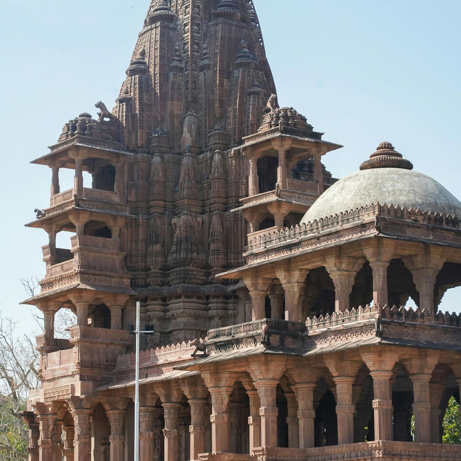 Intricately carved sandstone temple with domes and pillared balconies under clear sky, showcasing traditional Indian architecture and heritage grandeur