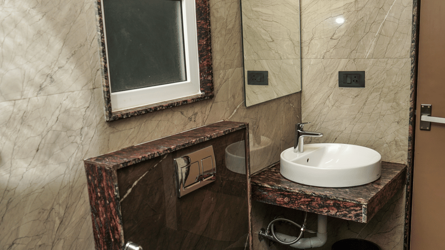 Compact and modern bathroom with a wall-mounted toilet, white ceramic basin, and neutral stone-effect wall tiles at Trident The Boutique Hotel, Ooty.