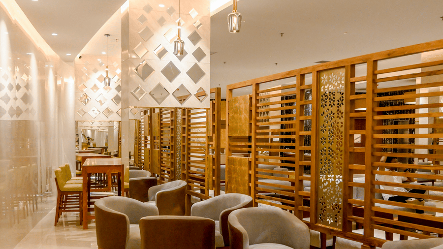 A long lounge area features multiple grey armchairs arranged in small conversational groups next to a wooden slatted partition wall at Tiara by MPS.