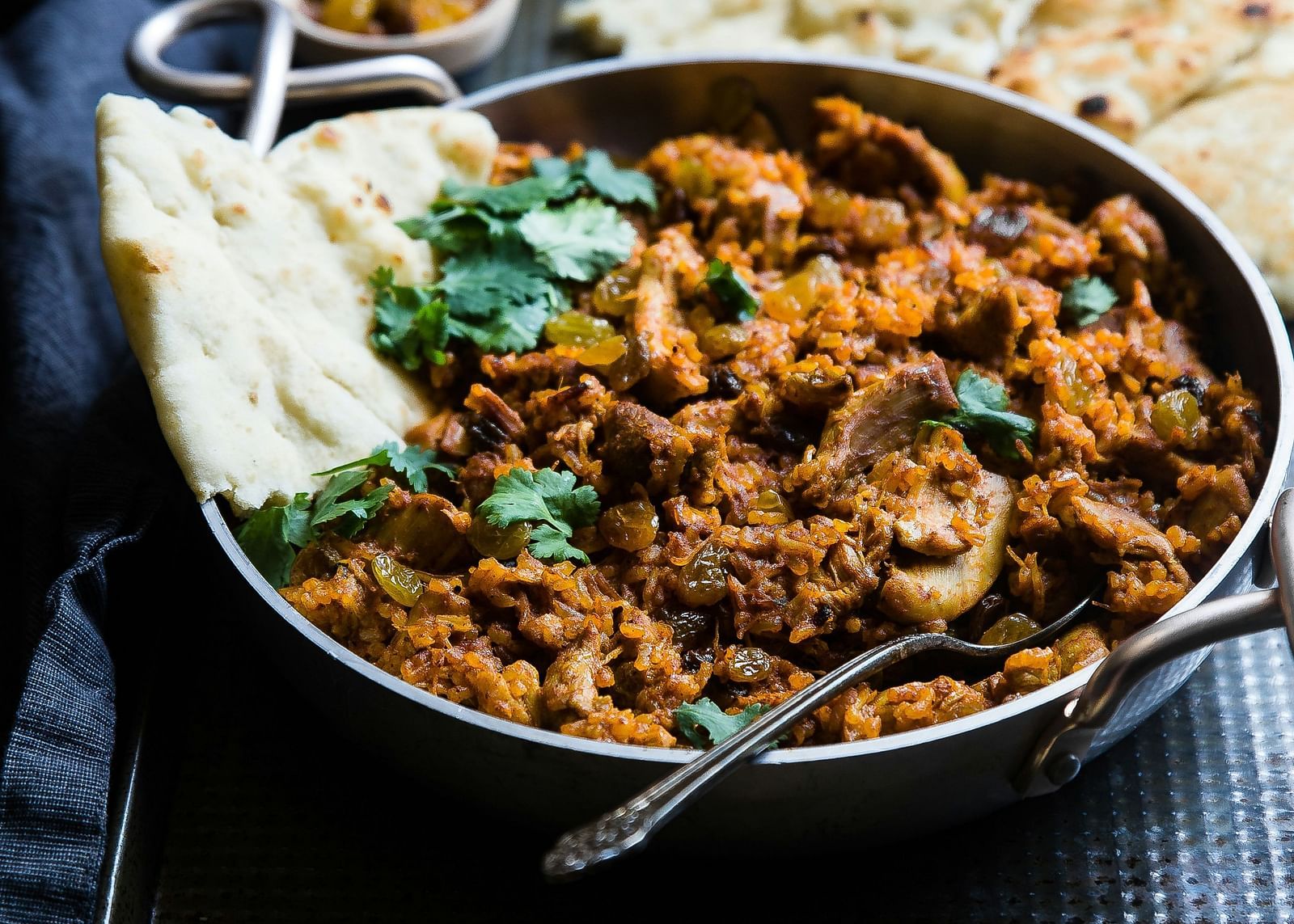 A bowl of Chicken Tikka Masala with Naan bread on a dark background.