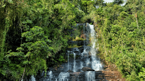 A waterfall cascading down the mountain under a partially cloudy, yet bright sky.
