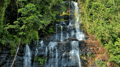 A waterfall cascading down the mountain under a partially cloudy, yet bright sky.