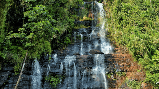A waterfall cascading down the mountain under a partially cloudy, yet bright sky.