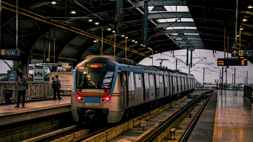 A metro train arriving at an elevated station platform while commuters wait alongside the tracks