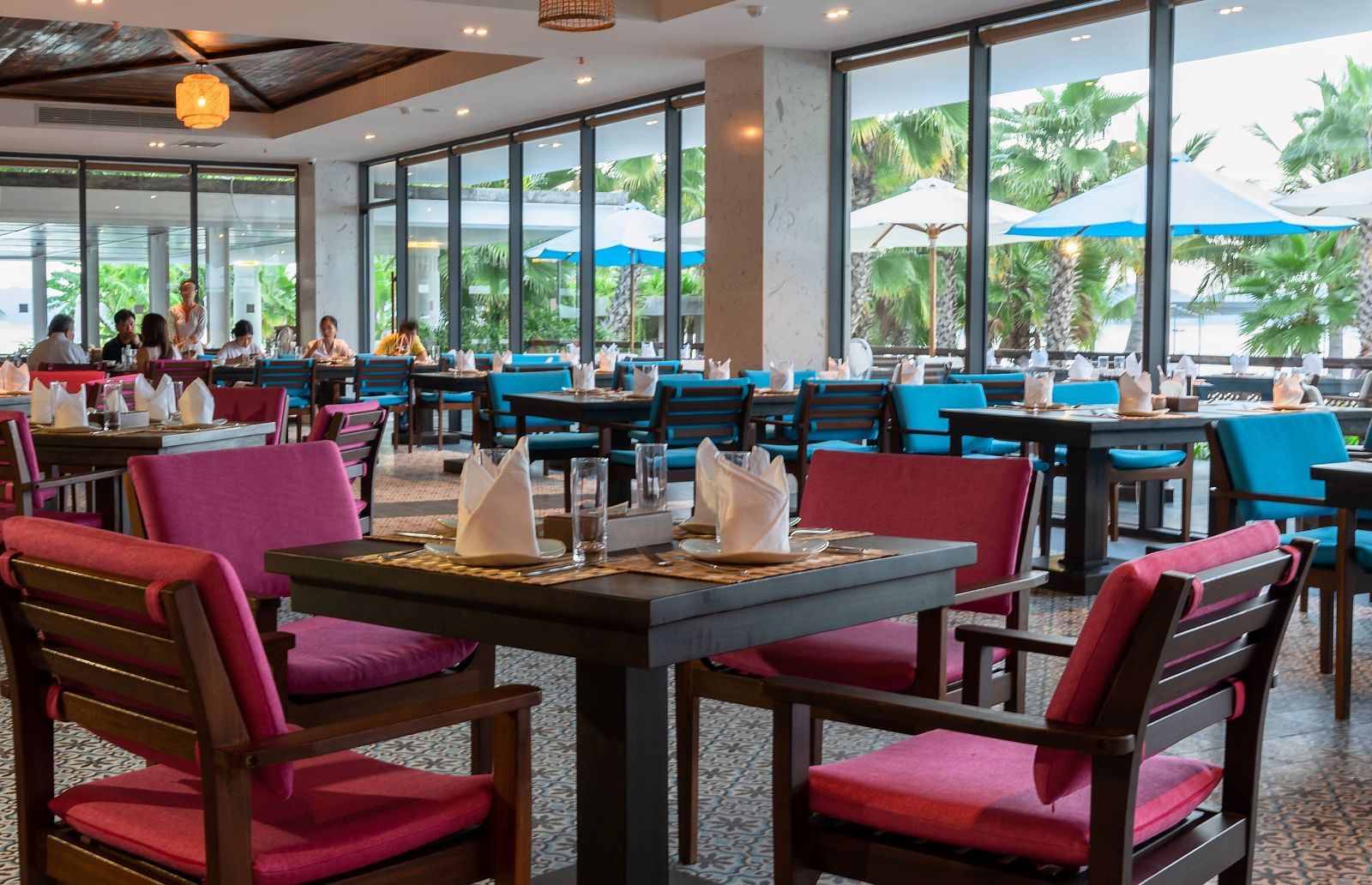 A view of our restaurant with comfortable seating arrangement, ambient lighting from hanging lamps and a glass door showcasing a great view - Alibu Resort Nha Trang