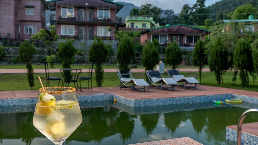 a pizza kept next to a beverage with the swimming pool in view - neer ganga Resorts