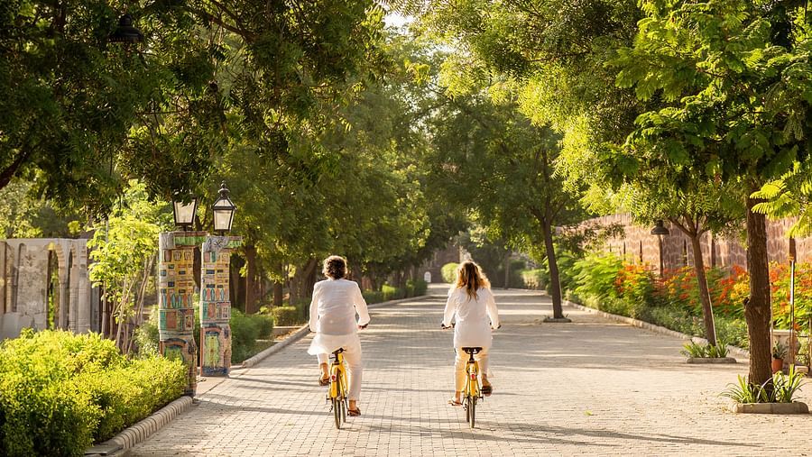 Two people cycling on an empty road with trees on the side at Surpura Bagh.