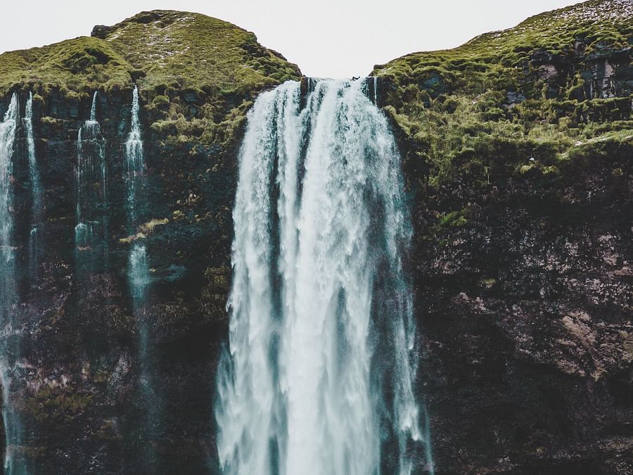 a cascading waterfall with greenery next to it  at Ibex River Resort, Pollachi